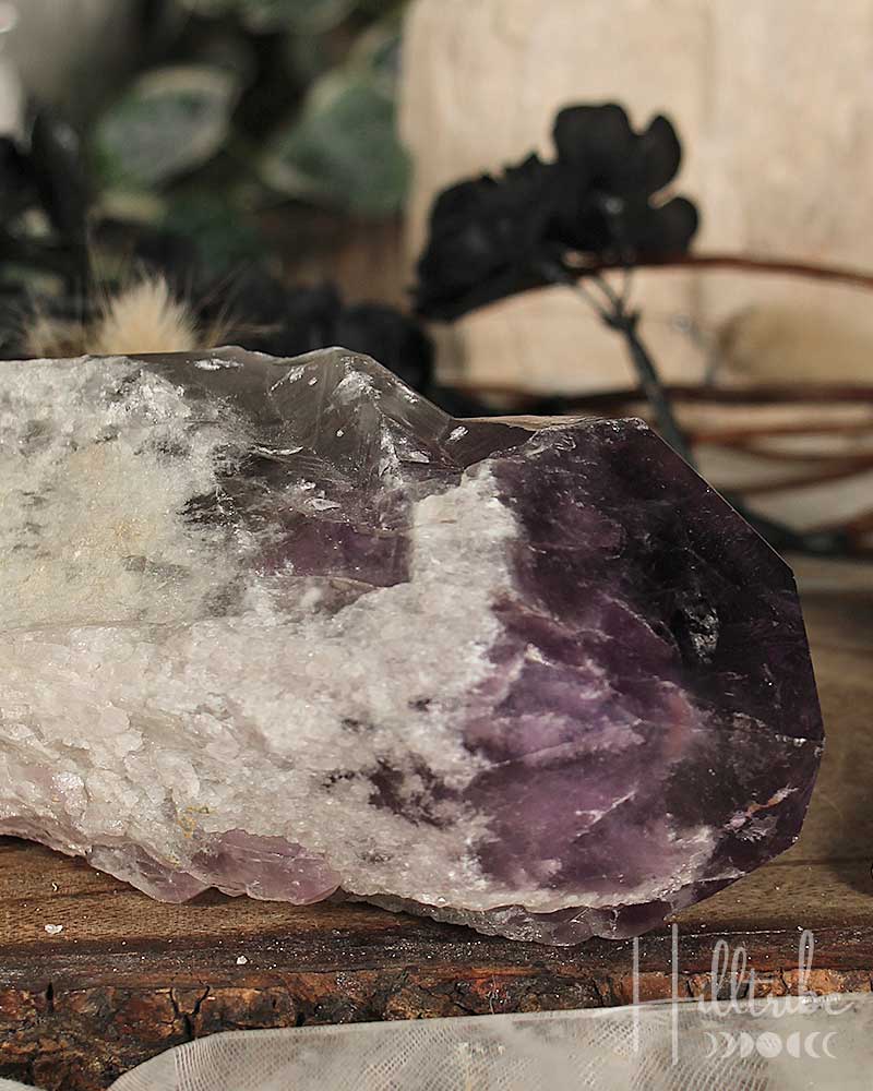 Close-up of a purple and white crystal on a wooden surface with blurred greenery in the background.