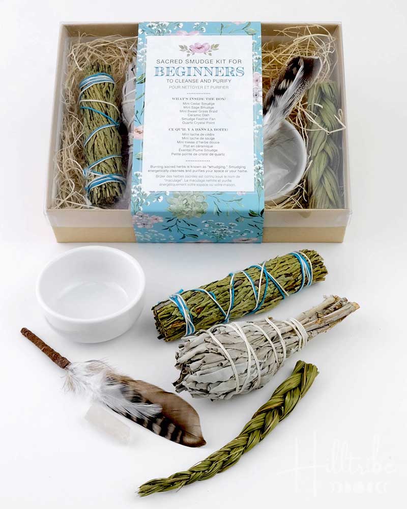 Smudging kit with sage sticks, feather, and candle on a white background
