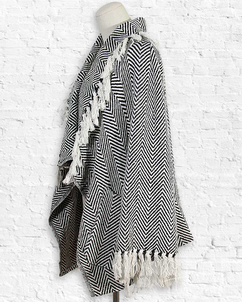 Black and white striped poncho with tassels on a mannequin against a textured white background