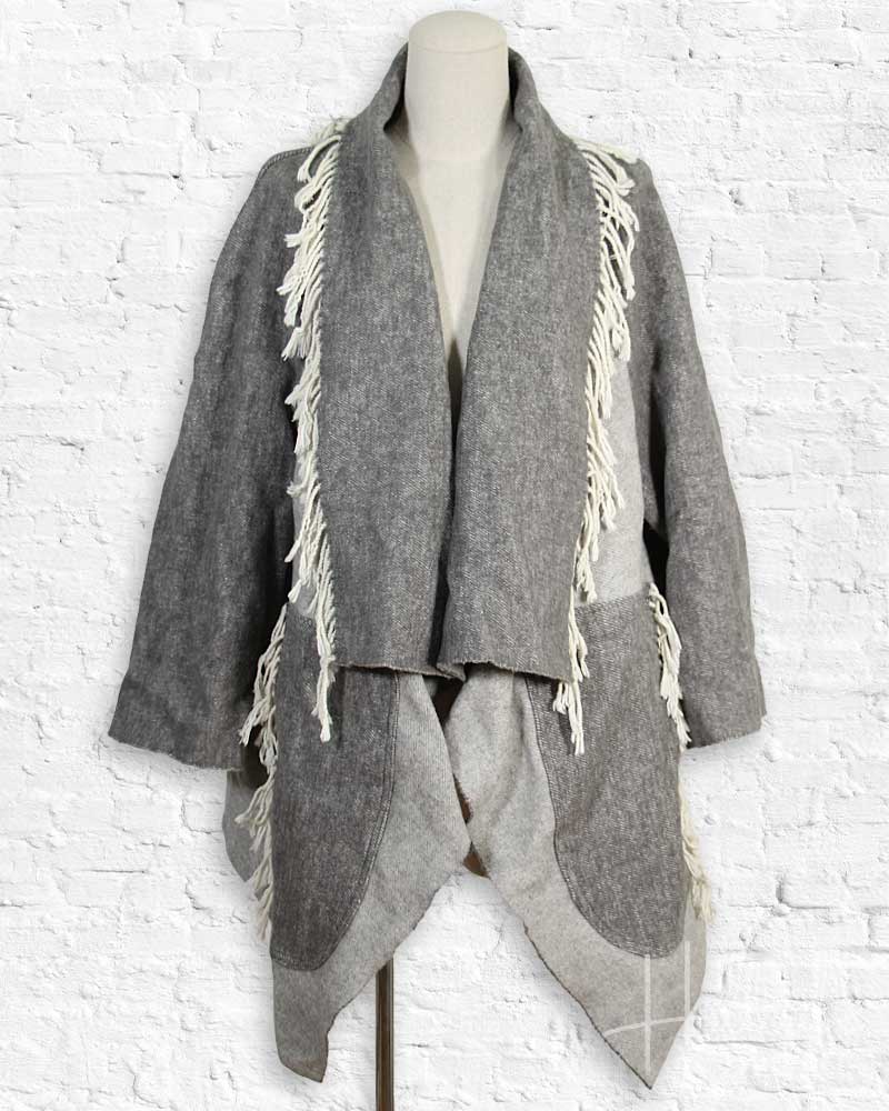 Gray textured jacket with fringe details on a mannequin against a white brick wall.