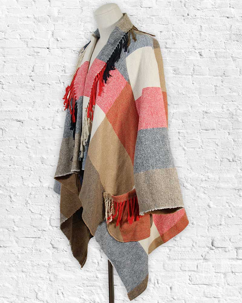 Colorful patterned scarf with fringes on a mannequin against a white brick wall.