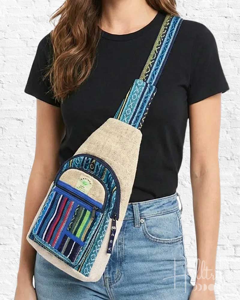 Person wearing a crossbody bag with blue and beige design against a white brick wall.