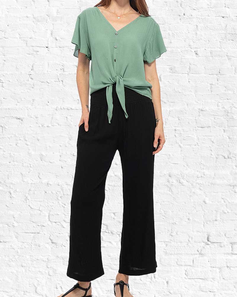 Person wearing a green top and black pants against a white brick wall.