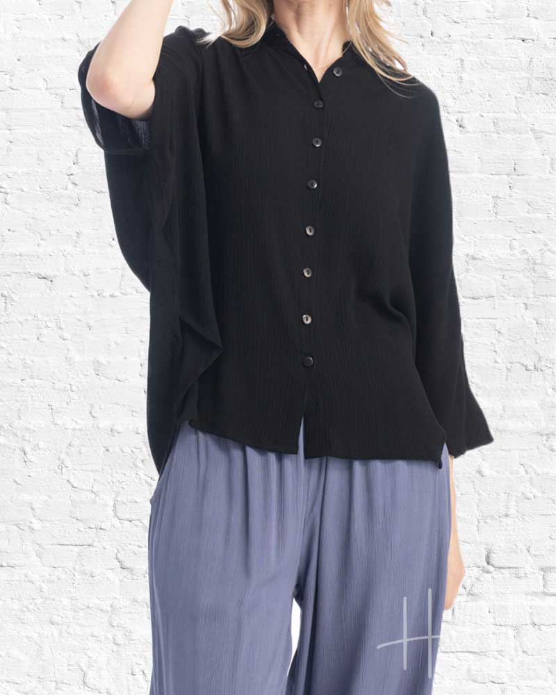 Person wearing a black button-up shirt and light blue pants against a white brick wall.