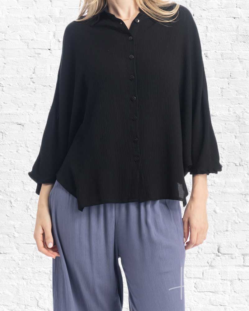 Person wearing a black shirt and gray pants against a white brick wall.