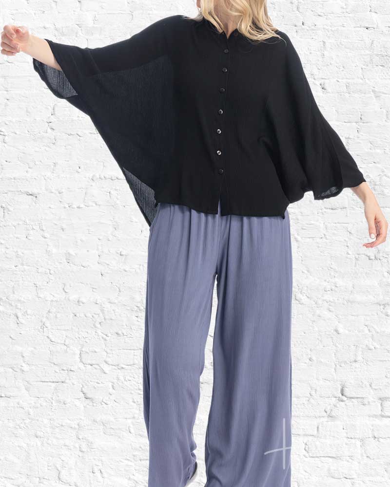 Person wearing a black top and gray pants against a white brick wall.