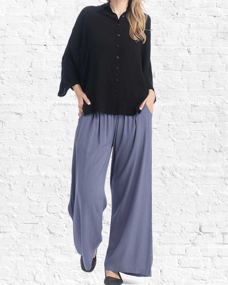 Person wearing a black shirt and gray wide-leg pants against a white brick wall.