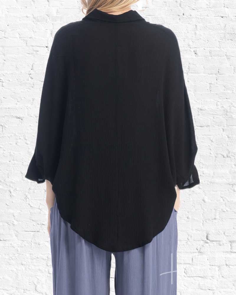 Person wearing a black oversized shirt and gray pants against a white brick wall.