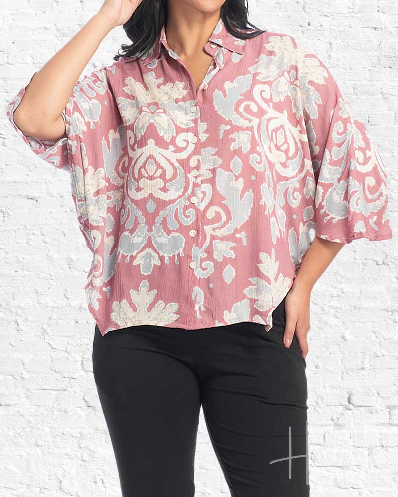 Woman wearing a pink floral blouse against a white brick wall.