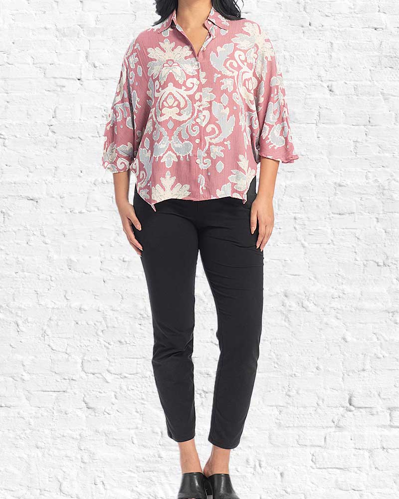Person wearing a pink floral blouse and black pants against a white brick wall.