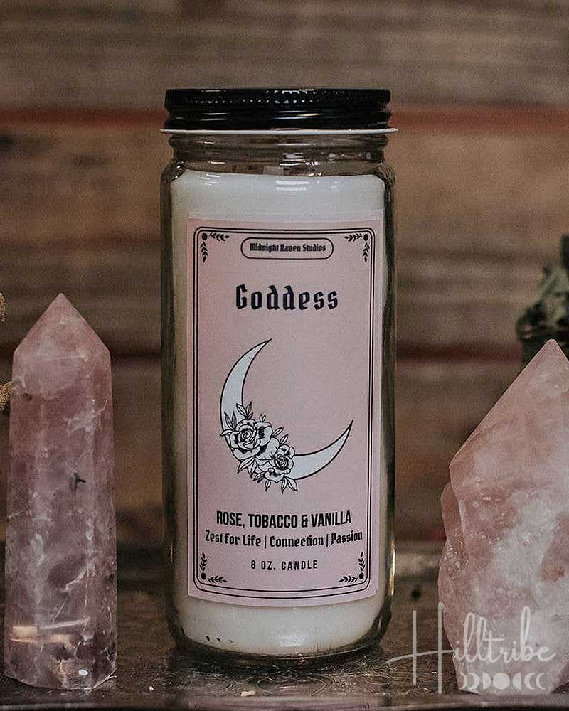 Candle labeled 'Goddess' with a pink label featuring a moon design, surrounded by crystals.