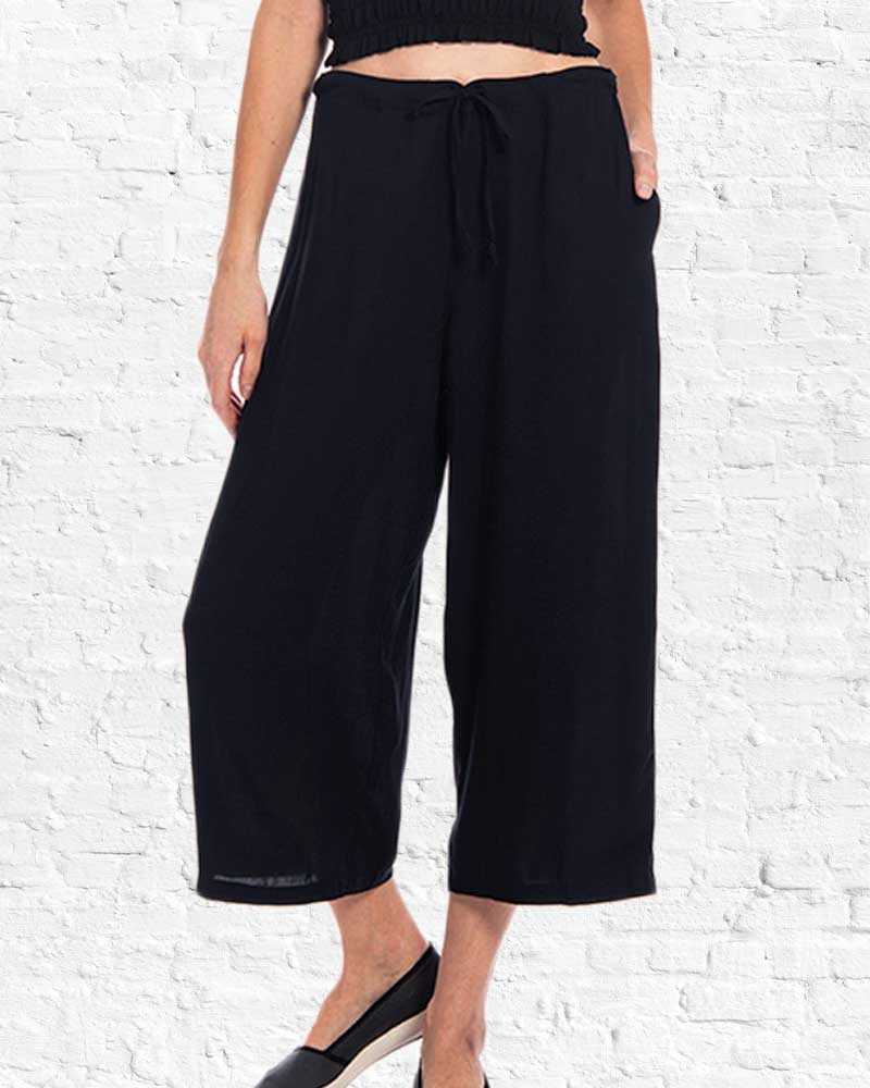 Person wearing black wide-leg pants against a white brick wall.