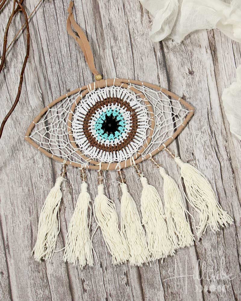 Dreamcatcher with eye design and tassels on a wooden surface