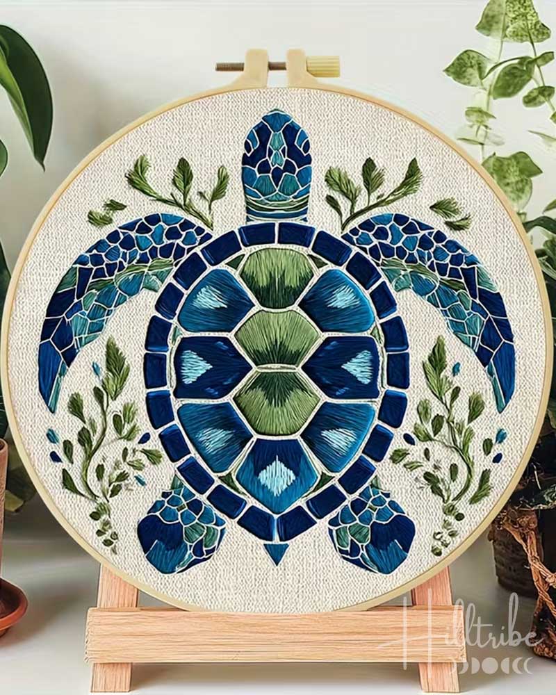 Embroidery hoop with a mosaic turtle design surrounded by green leaves.