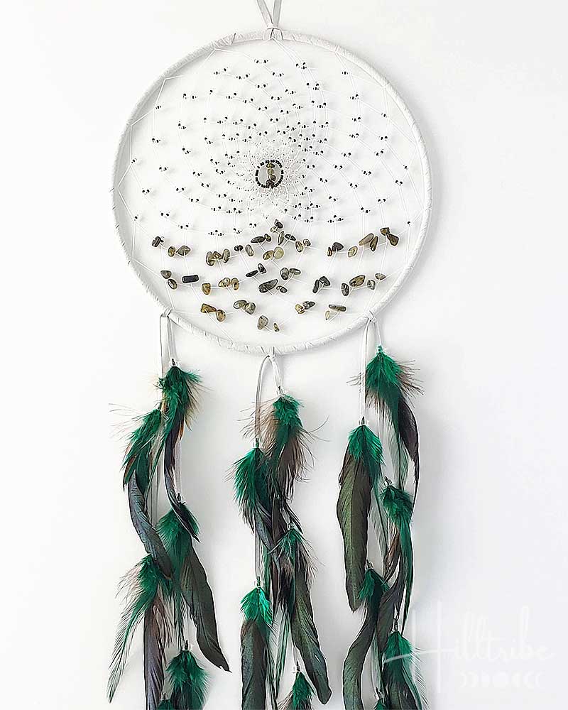 White dreamcatcher with green feathers on a white background