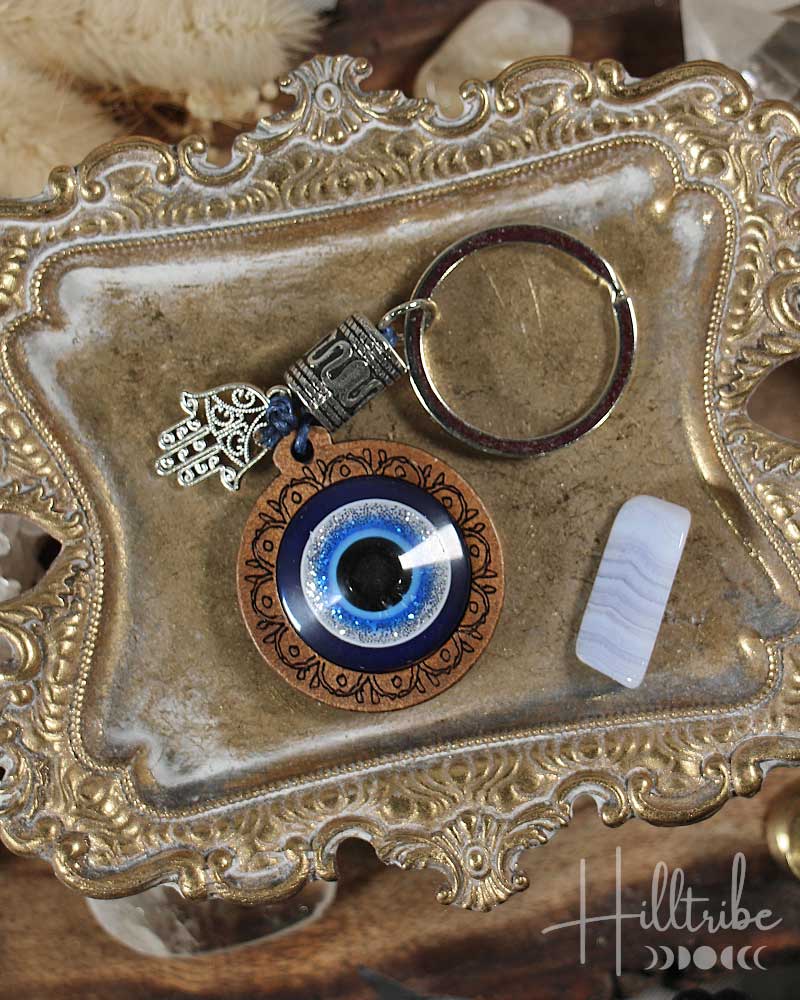 Keychain with evil eye design on a decorative metal tray, featuring the brand 'Hilltribe'.