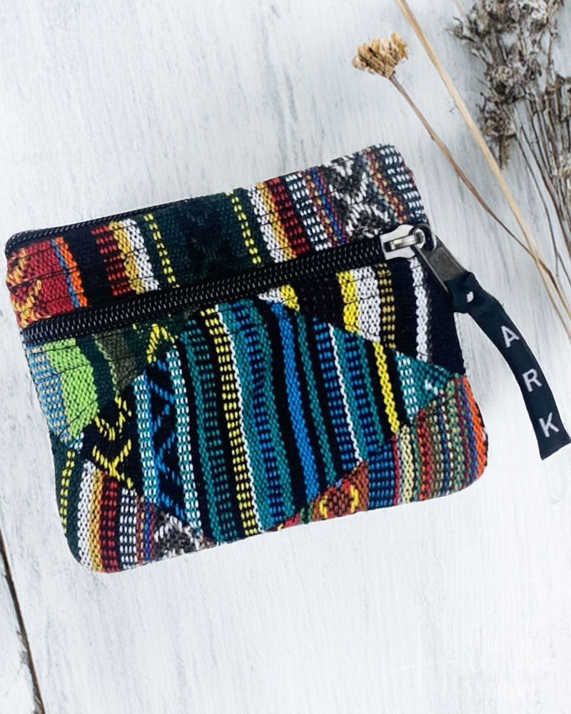 Colorful woven pouch with a visible brand name on a light wooden surface.