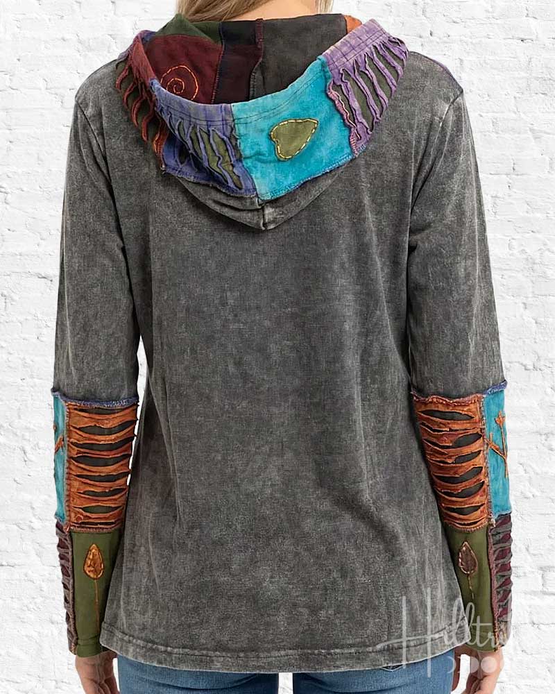 Gray hoodie with colorful patchwork design on a white brick wall background