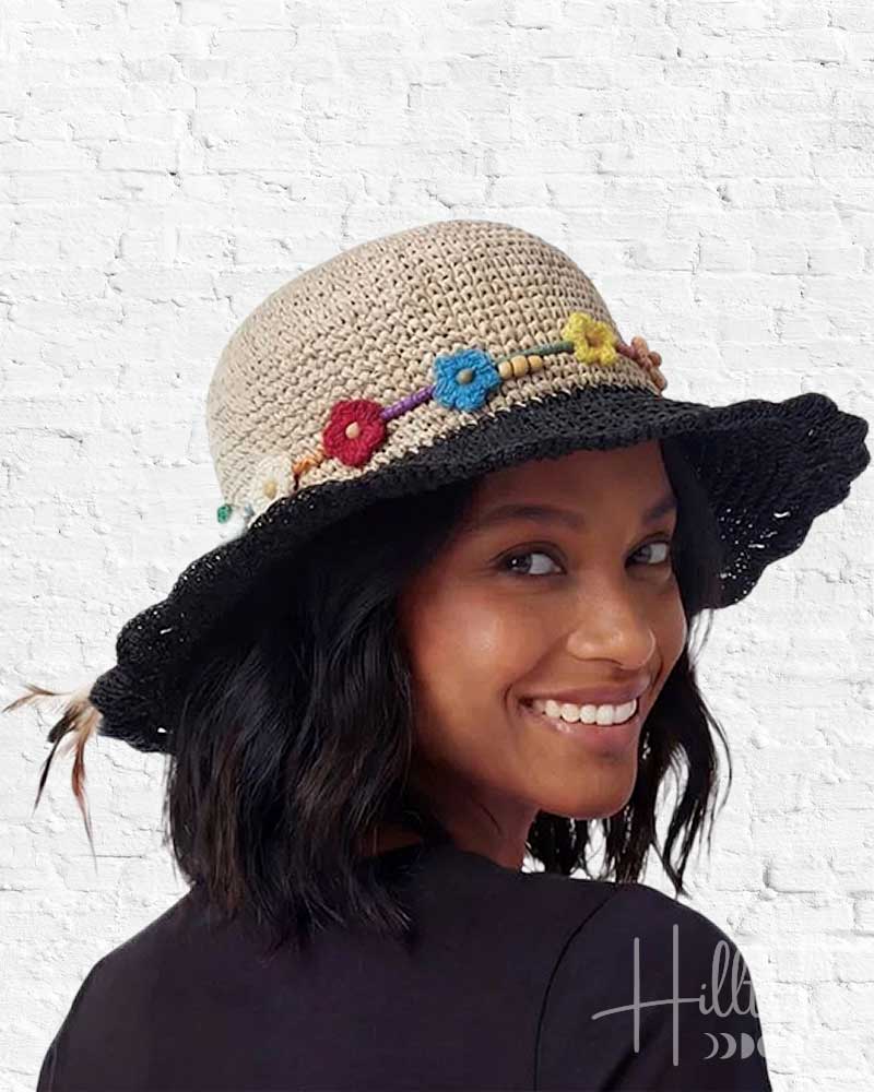 Woman wearing a decorative hat with colorful flowers against a white brick wall