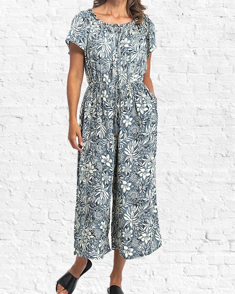 Woman wearing a floral jumpsuit against a white brick wall.