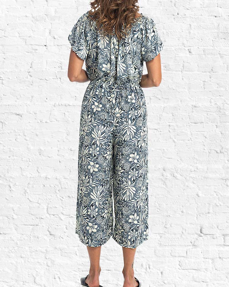 Person wearing a floral jumpsuit against a white brick wall.