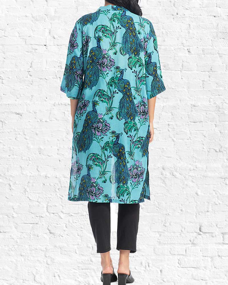 Person wearing a teal floral patterned shirt against a white brick wall.