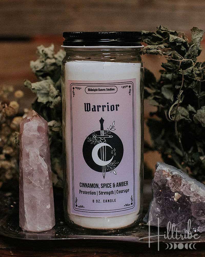 A jar candle labelled 'Warrior', placed on a dark tray with crystals and dried botanicals against a rustic wooden background.