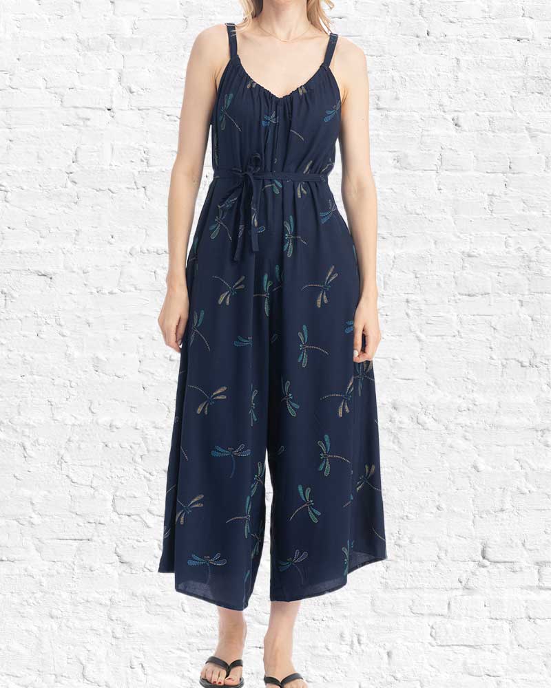 Navy blue jumpsuit with dragonfly pattern worn by a person against a white brick wall.