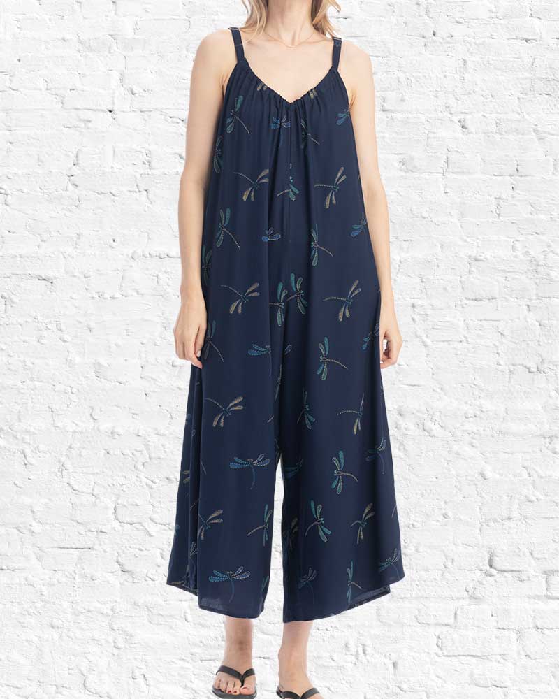 Navy blue jumpsuit with dragonfly pattern worn by a person against a white brick wall.