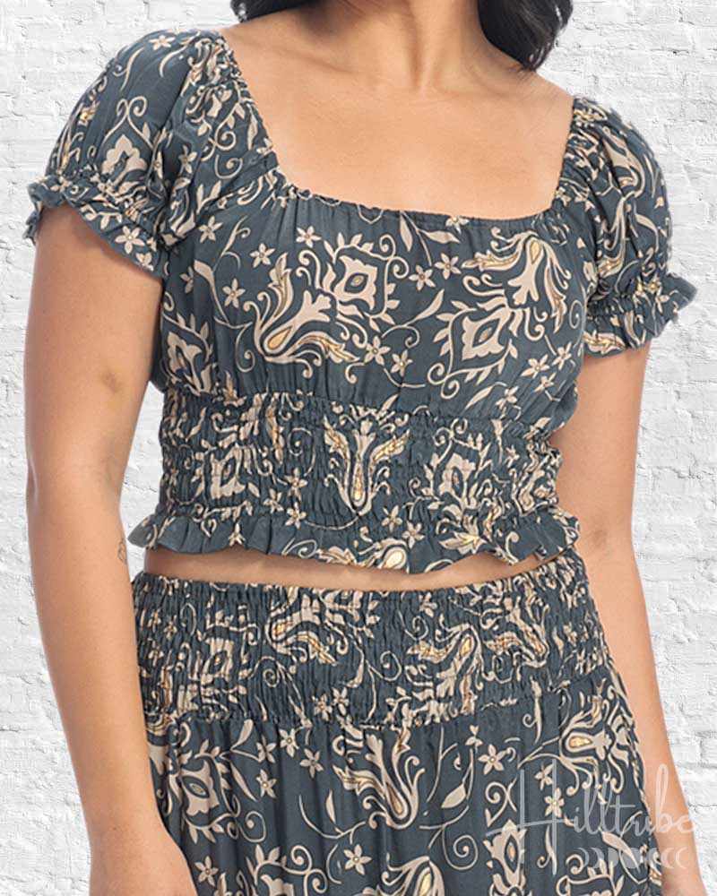 Woman wearing a patterned top and skirt set against a white brick wall.