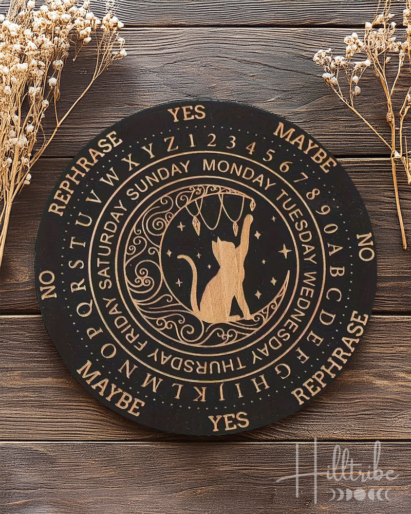 Decorative pendulum board with a cat and astrological design and text on a wooden surface with dried flowers.