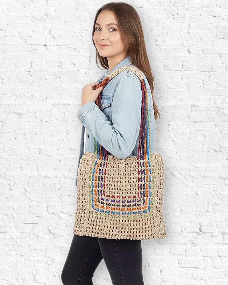 Woman holding a colorful woven bag against a white brick wall