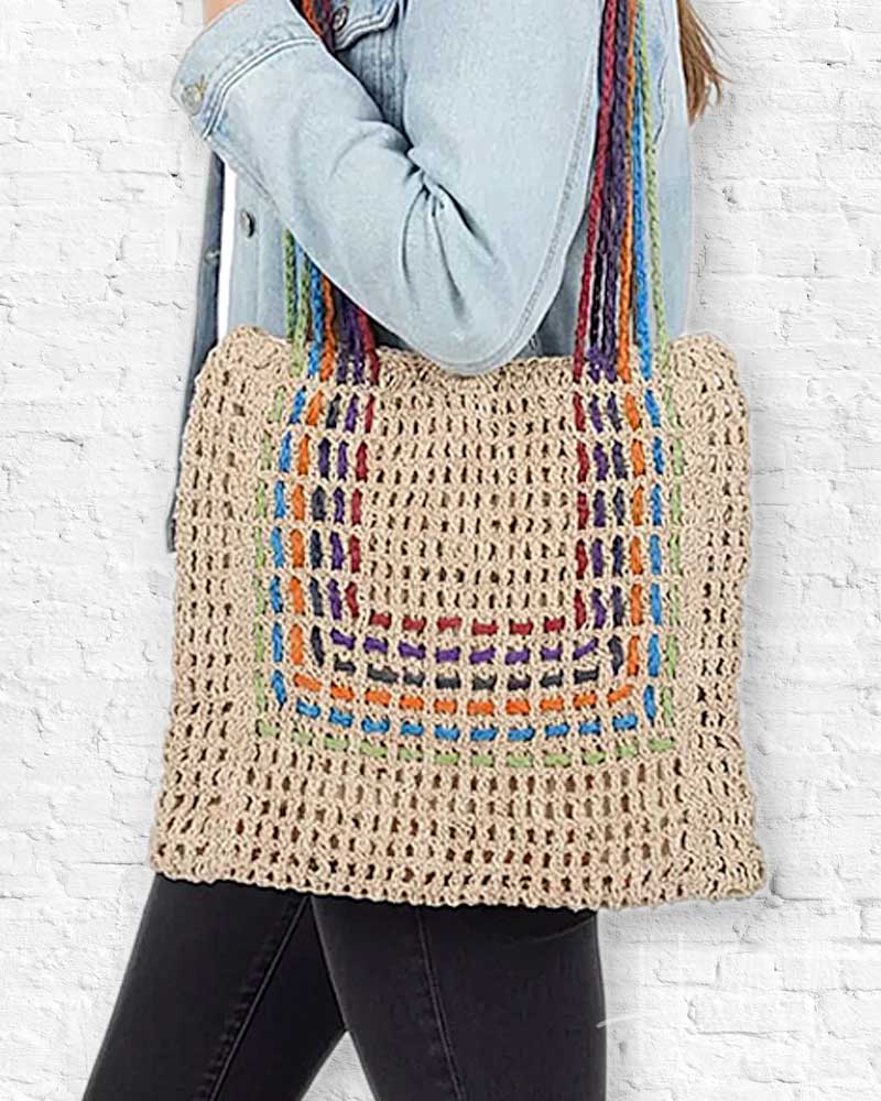 Person holding a crocheted bag with colorful handles against a white brick wall.