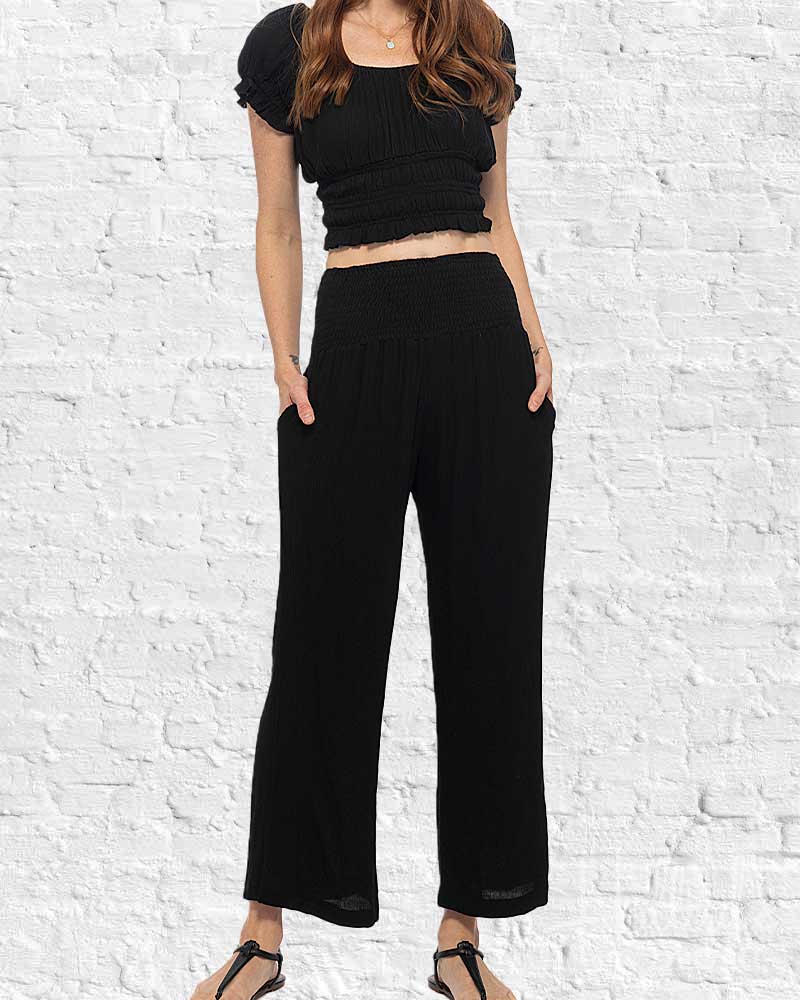 Person wearing a black crop top and wide-leg pants against a white brick wall.