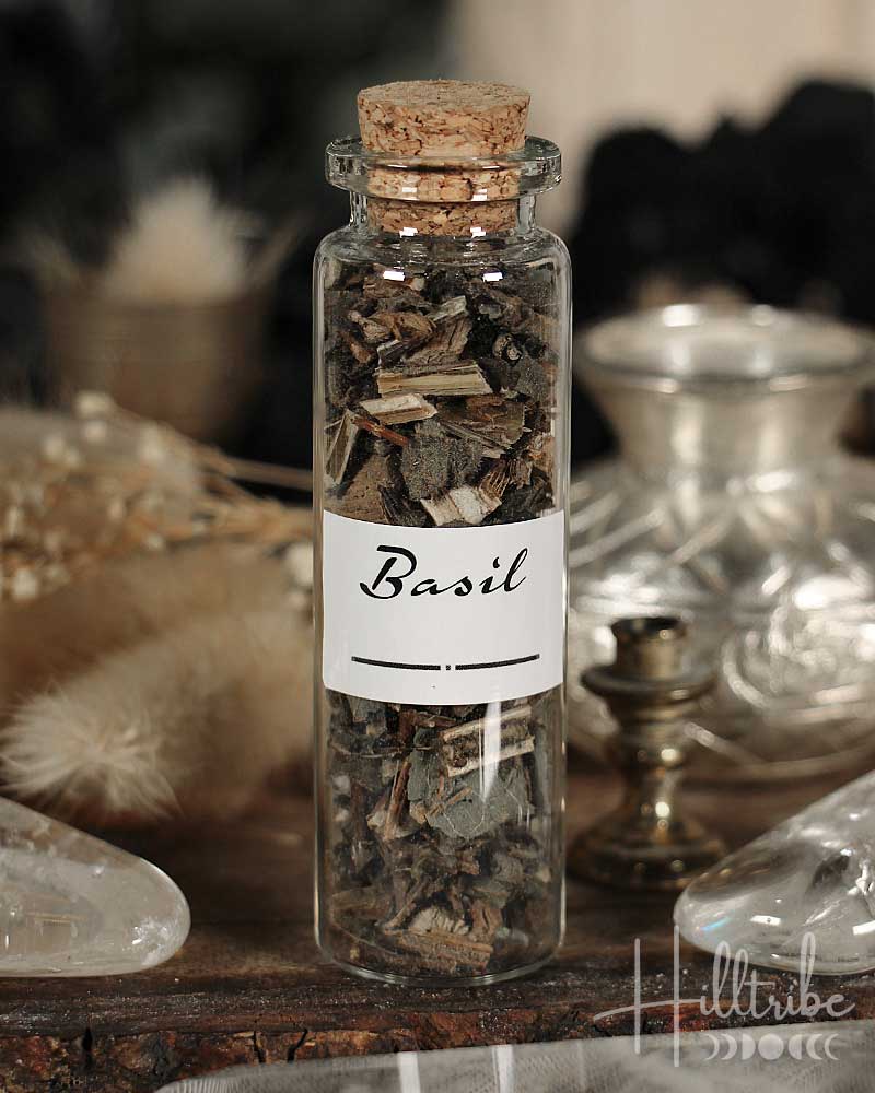 Glass bottle with cork lid containing dried basil leaves on a wooden surface.