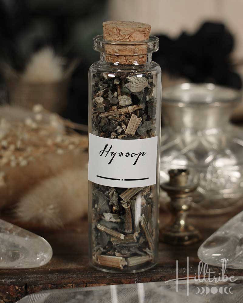 Glass bottle with cork lid containing herbs labeled 'Hyssop' on a wooden surface.