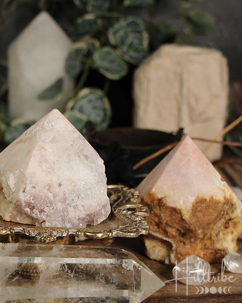 Two Rose Amethyst with Jasper Cut Base pyramids on a reflective surface with blurred greenery in the background