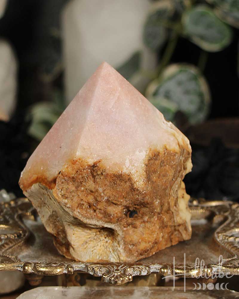 Rose Pink Amethyst Cut Base crystal on a decorative stand with blurred greenery in the background
