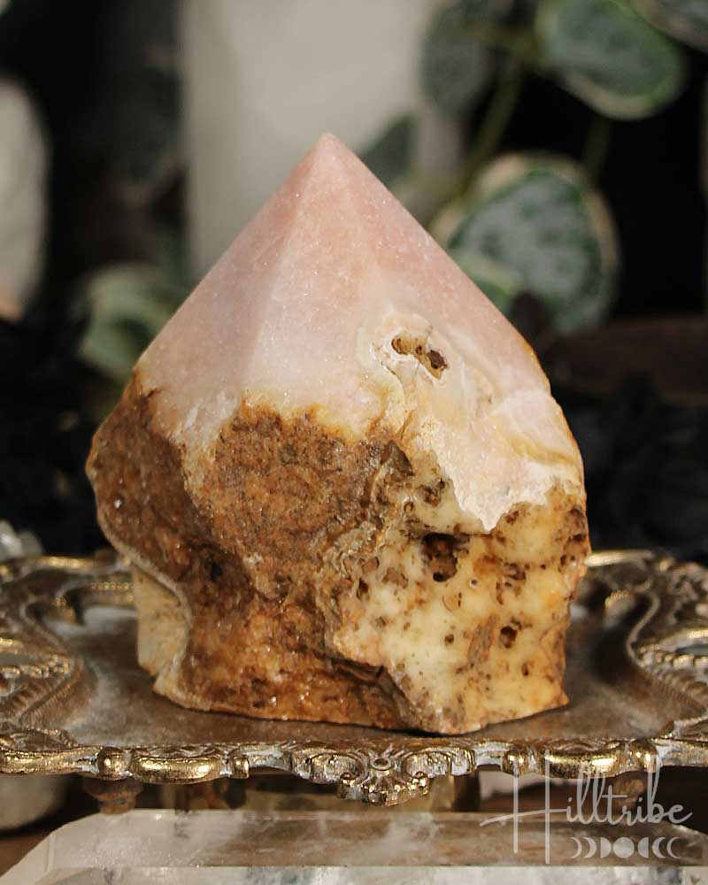 Rose Pink Amethyst Cut Base crystal on a decorative stand with blurred greenery in the background