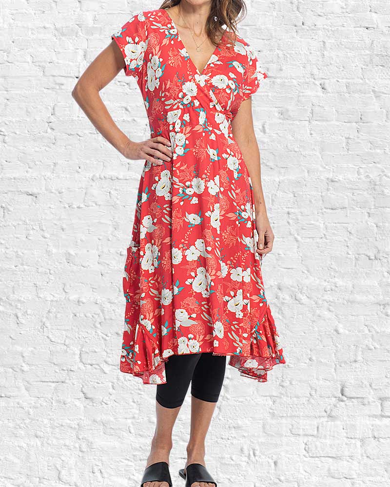 Woman wearing a red floral dress against a white brick wall.
