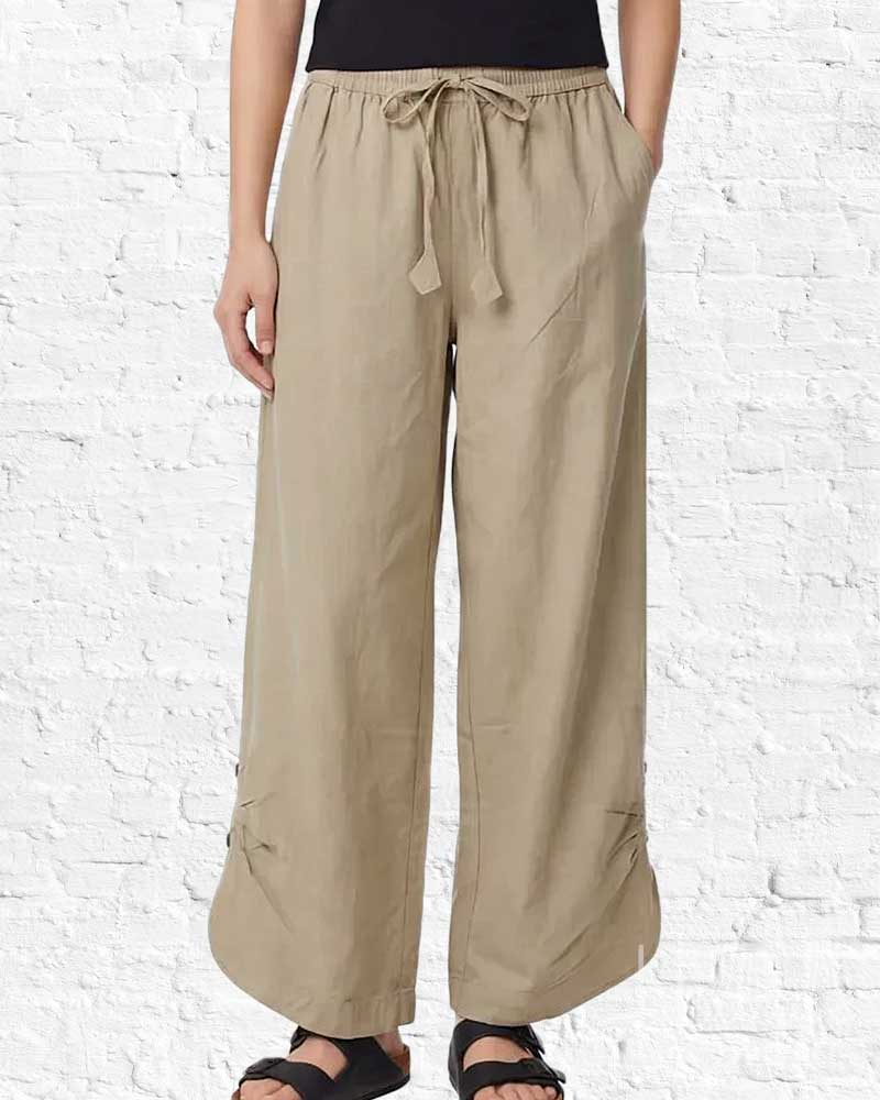 Beige wide-leg pants worn by a person on a white brick wall background