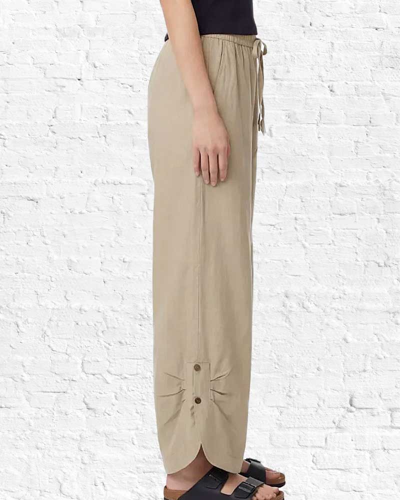 Beige wide-leg pants with buttons on a white brick wall background