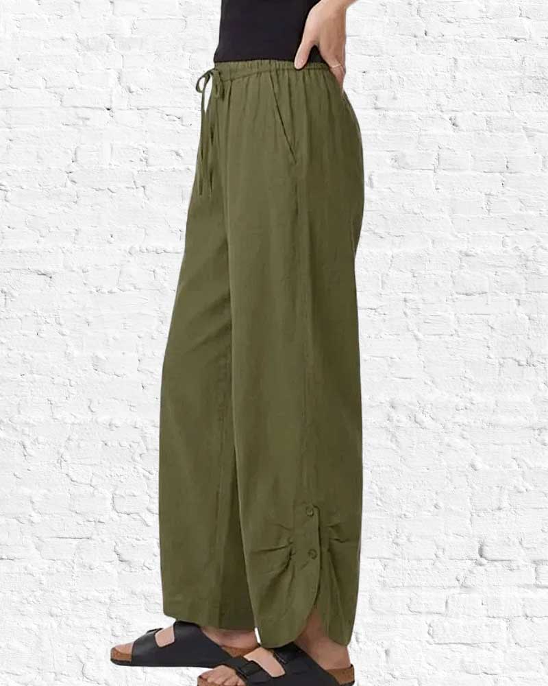 Person wearing olive green wide-leg pants against a white brick wall.