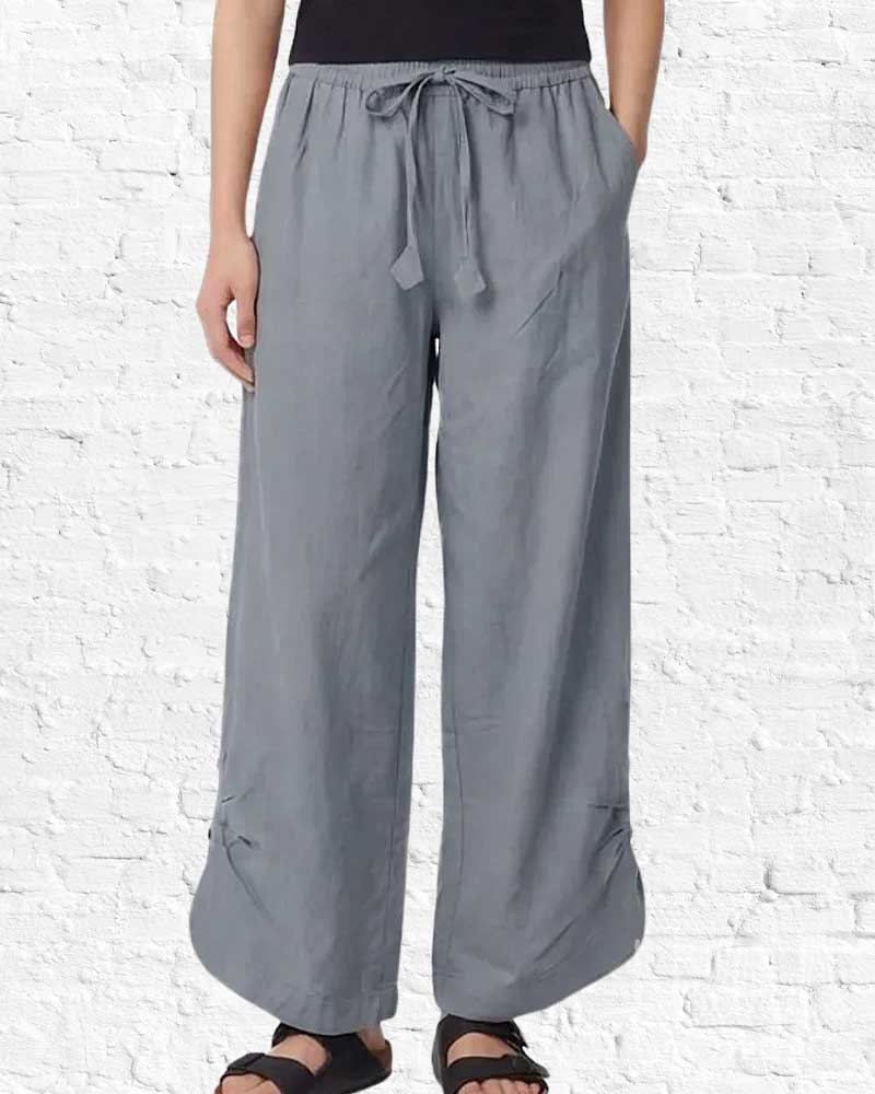 Person wearing gray wide-leg pants on a white brick wall background