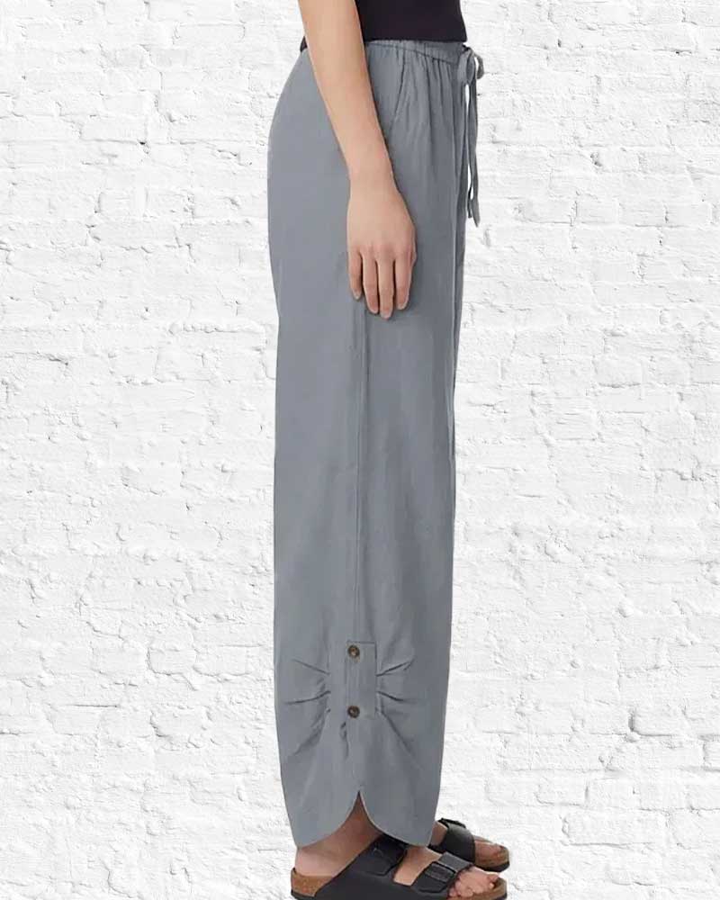 Person wearing gray pants with buttons against a white brick wall.