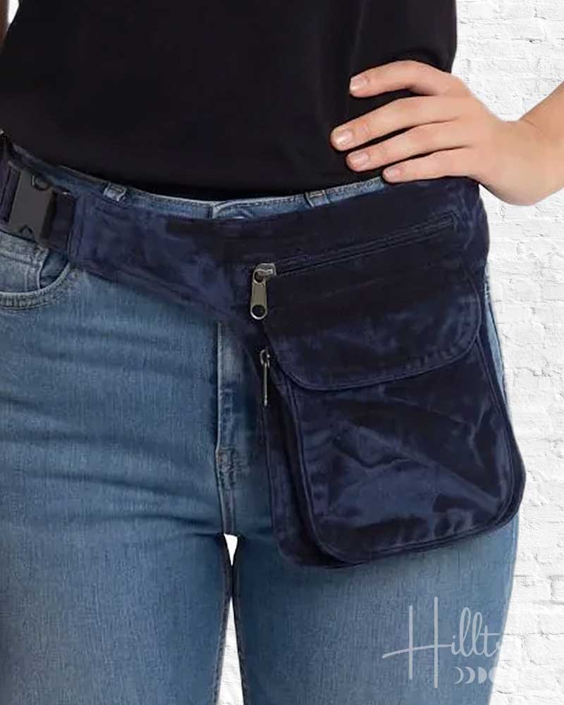 Navy waist bag worn by a person with blue jeans against a white brick wall.