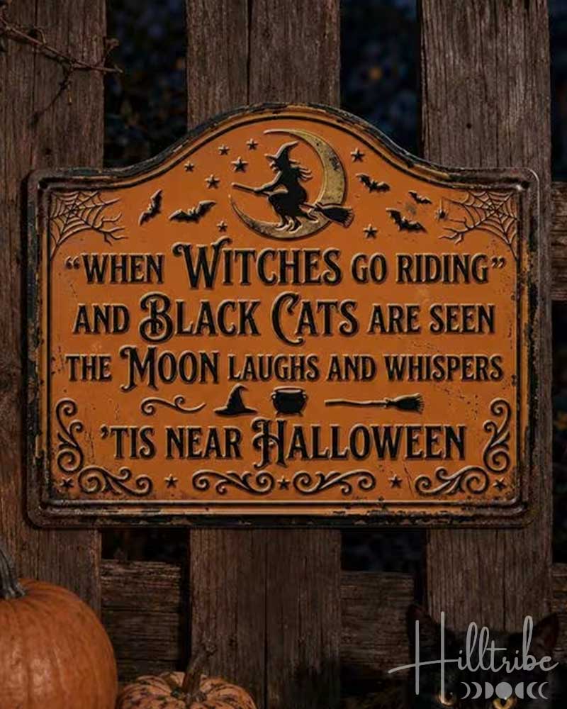 A Halloween decorative sign with a rustic orange-brown background and black lettering that reads, "When Witches Go Riding and Black Cats Are Seen The Moon Laughs and Whispers 'Tis Near Halloween." The sign is mounted on a weathered wooden fence at night, with a lit lantern, pumpkins, and a black cat nearby.