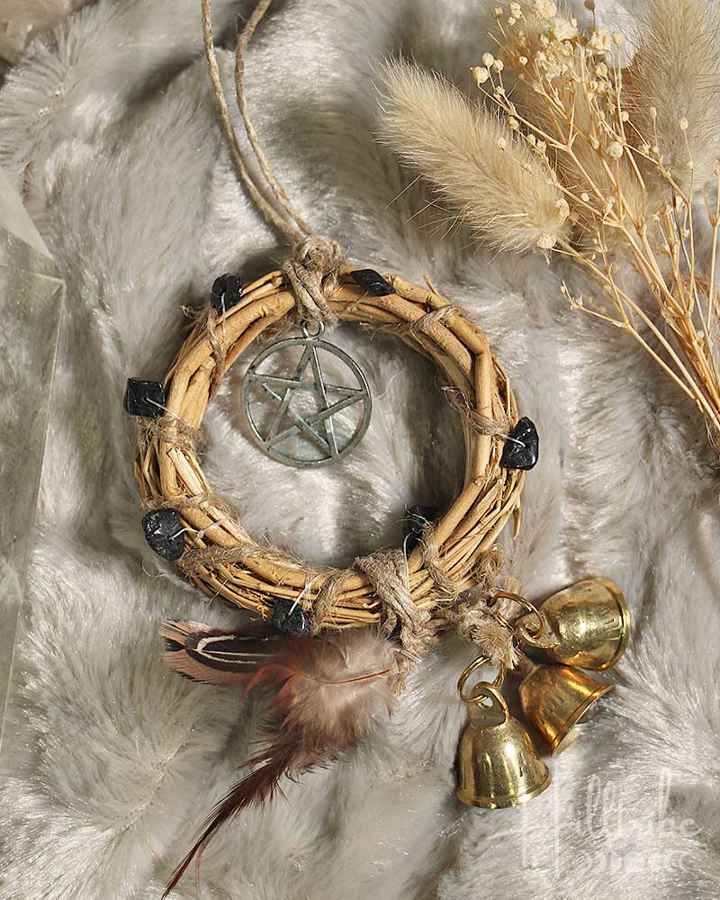 Decorative wreath with pentacle pendant, feathers, and bells on a textured surface