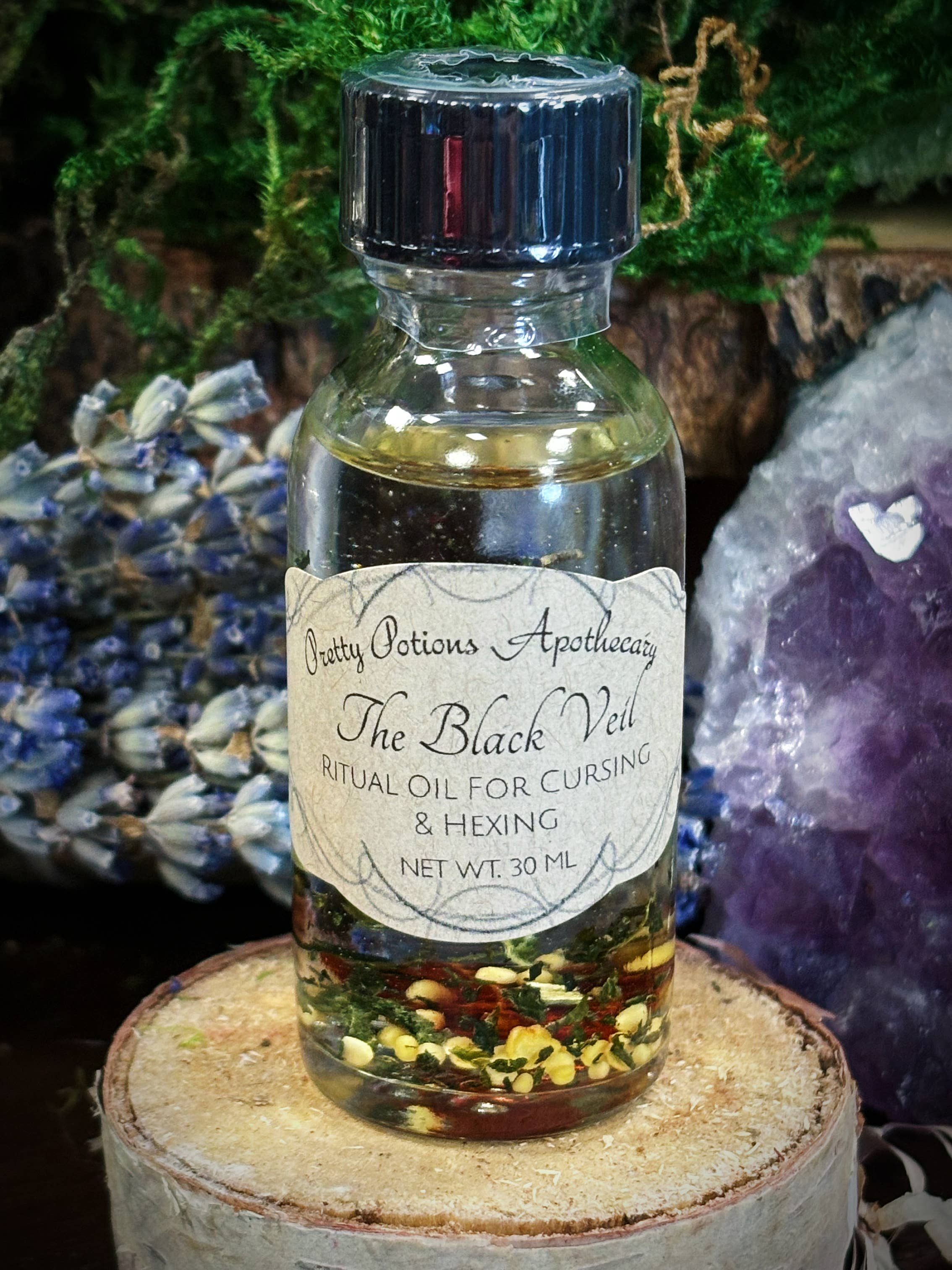Bottle of 'The Black Veil' ritual oil for cursing and hexing on a wooden surface with a natural background.