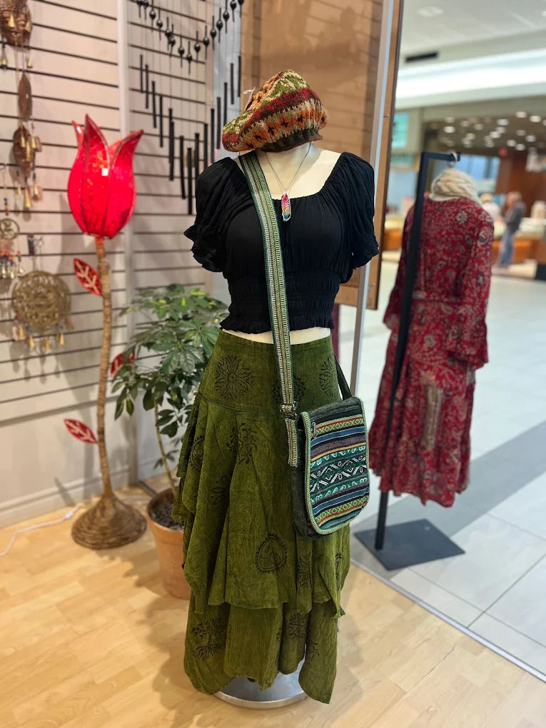 Mannequin wearing a green skirt, black top, and colorful bag in a store setting.